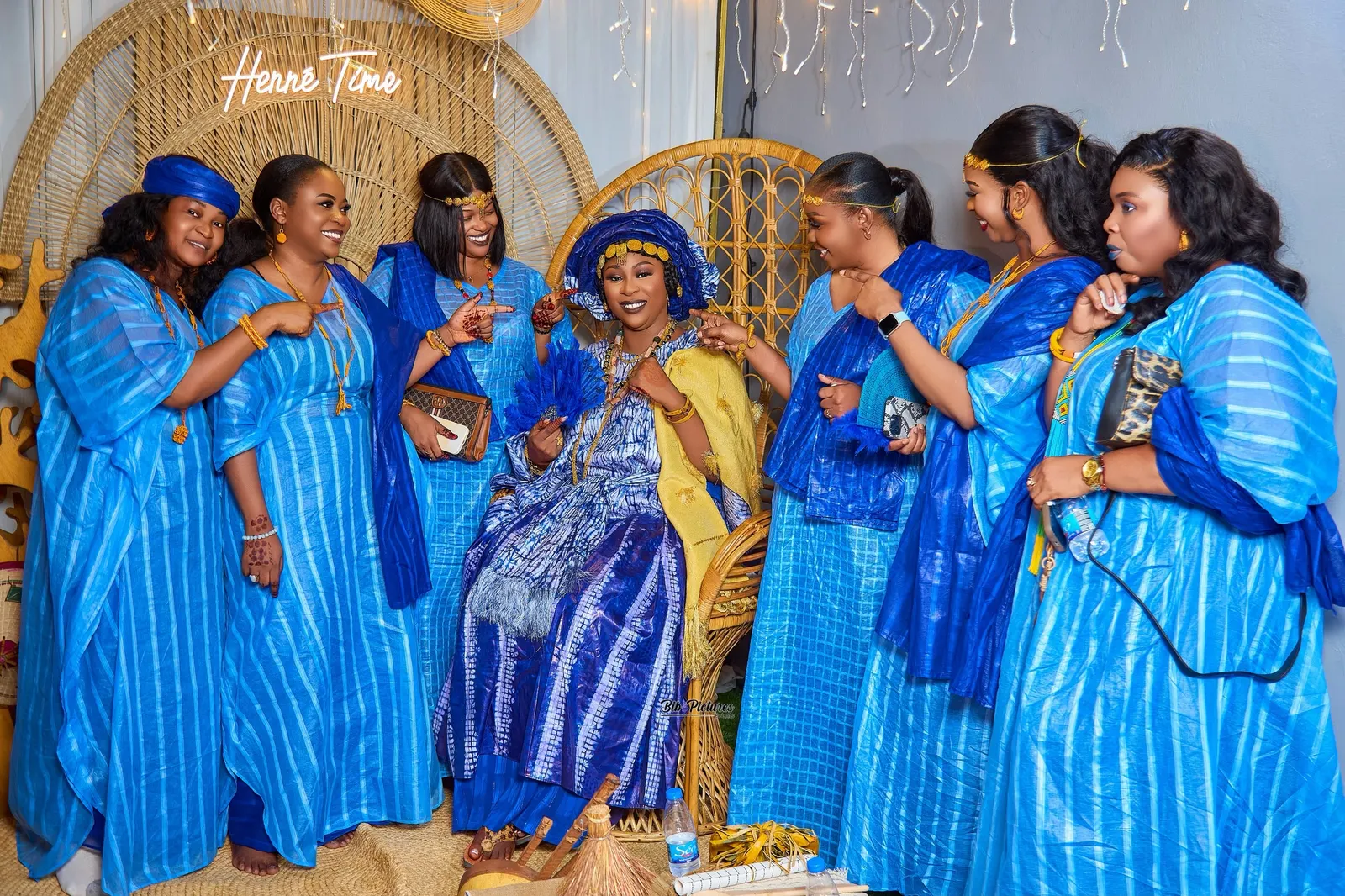 Photo de groupe, Henné Time : la mariée en bleu et wax, châle jaune, amies en bleu, décor en rotin.